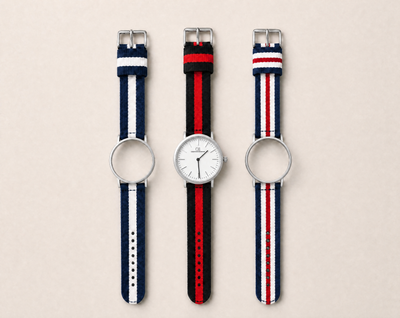 Tela Swiss Made modular watch — round silver case with white dial, shown with three interchangeable nato straps in navy-white, black-red and navy-red-white